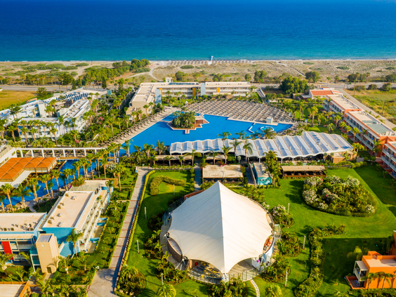 Een luchtfoto van het uitgestrekte Blue Lagoon Resort, waarop de zwembaden, de tuinen, de gebouwen en de ligging direct aan het strand van Kos te zien zijn.