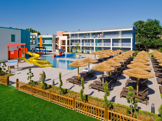 Het vrolijke kinderzwembad van Blue Lagoon Resort op Kos, met kleine gele glijbanen en rijen ligbedden met rieten parasols voor de ouders.