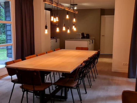Lange, houten eettafel voor grote groepen in de eetkamer van een groepsaccommodatie op Bospark de Schaapskooi.