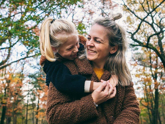 Een lachende moeder knuffelt haar dochter in een sfeervol bos met herfstkleuren op de Veluwe.