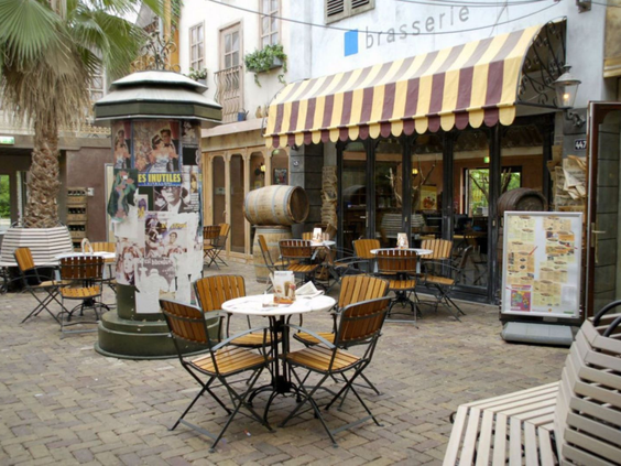 Het gezellige, lege terras van de brasserie op Bospark De Schaapskooi, met een geel-gestreepte luifel.