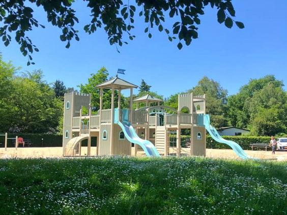 Groot houten speelkasteel met meerdere glijbanen in de buitenspeeltuin van Bospark de Schaapskooi op de Veluwe.