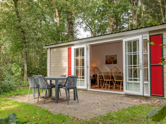 Een vrijstaand vakantiehuisje op Bospark Lunsbergen met openslaande deuren naar het terras, gelegen in het bos en omgeven door gras en bomen.