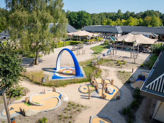 Overzicht van de centrale buitenspeeltuin en het terras bij Bospark Lunsbergen, met diverse speeltoestellen, zand en een interactieve Sona dansboog.