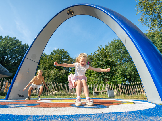 Twee blije kinderen springen en dansen op de interactieve Sona dansboog, een speeltoestel met geluid en spelletjes bij Bospark Lunsbergen in Drenthe.