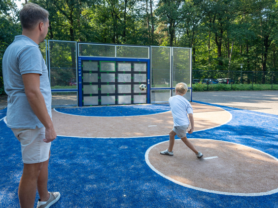 Vader en zoon spelen samen bij de interactieve Sutu voetbalmuur op het multifunctionele sportveld van Bospark Lunsbergen.