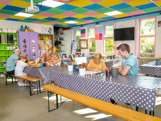 Kinderen en ouders knutselen gezellig samen aan lange tafels in de kleurrijke Kids Club van Bospark Lunsbergen.