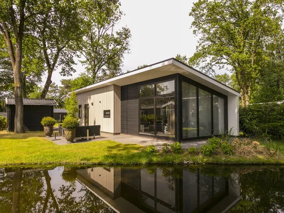 Een moderne design vakantiewoning met grote ramen, direct gelegen aan de waterkant en weerspiegeld in de vijver van Bospark Markelo.