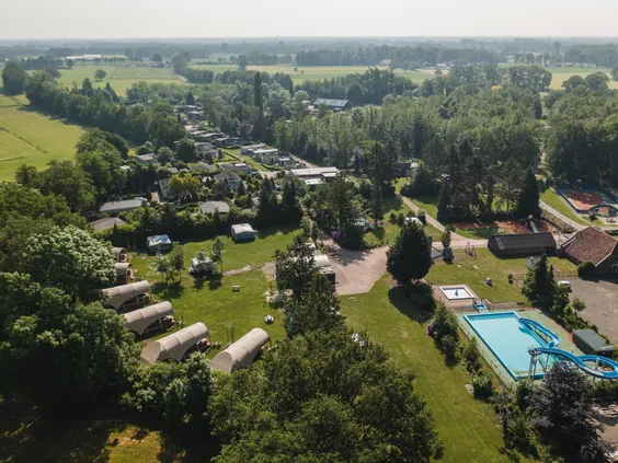 Luchtfoto van het groene en ruim opgezette Bospark Markelo, met een duidelijk zicht op het zwembad, de vakantiehuisjes en de omliggende natuur.