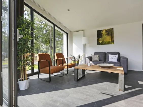 Stijlvolle, lichte woonkamer van een vakantiehuis op Bospark Markelo, met een comfortabele zithoek en een grote glazen pui naar buiten.