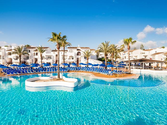 Het grote, helderblauwe hoofdzwembad van Bouganvilla Hotel & Appartementen op Mallorca, omringd door witte gebouwen en palmbomen.