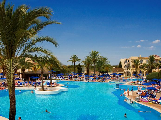 Zonnig overzicht van het lagune-stijl zwembad bij Bouganvilla in Sa Coma, met veel ligbedjes en gasten die genieten van het water.