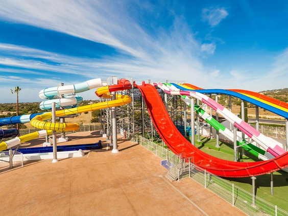 Groot overzicht van het waterpark bij Bouganvilla met een veelvoud aan kleurrijke en spectaculaire waterglijbanen tegen een helderblauwe lucht.