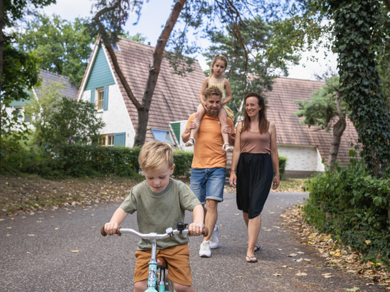 Gezin met jonge kinderen wandelt en fietst over een pad op vakantiepark De Katjeskelder.