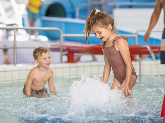 Twee jonge kinderen spelen en spetteren met water in het ondiepe peuterbad van het zwembad op Bungalowpark De Katjeskelder.
