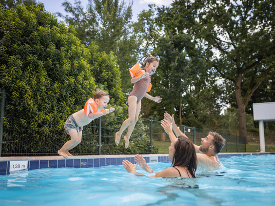 Twee kinderen met zwemvleugels springen in het buitenzwembad, waar hun ouders ze opwachten, op een zonnige dag bij De Katjeskelder.