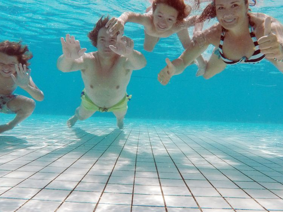 Lachende kinderen zwemmen en zwaaien onder water in het heldere zwembad van Bungalowpark Hoenderloo op de Veluwe.