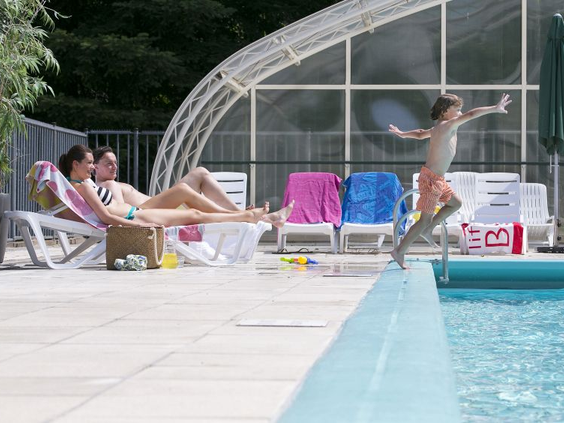Een kind maakt een bommetje in het buitenzwembad van Bungalowpark Hoenderloo, terwijl de ouders op ligbedden ontspannen.