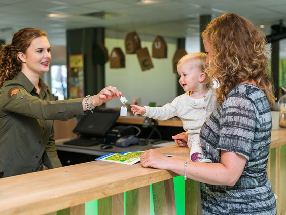 Een moeder en kind worden vriendelijk ontvangen en checken in bij de receptie van Bungalowpark Hoenderloo.