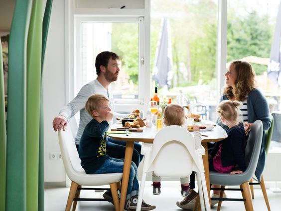 Een gezin met kinderen geniet samen van een maaltijd aan een tafel in het gezellige restaurant van Bungalowpark Hoenderloo.