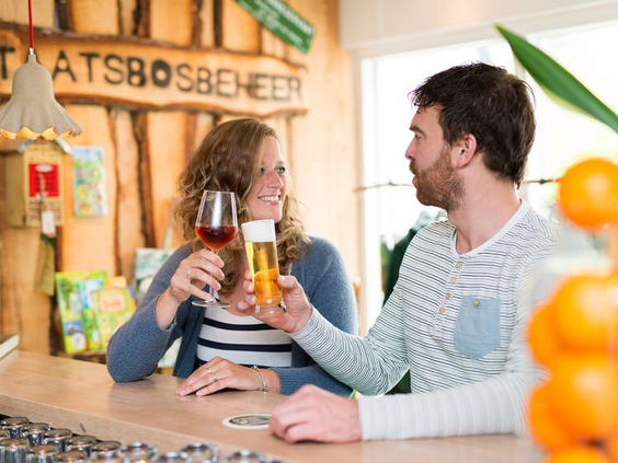Een man en vrouw proosten met een drankje aan de bar in het gezellige restaurant van Bungalowpark Hoenderloo.