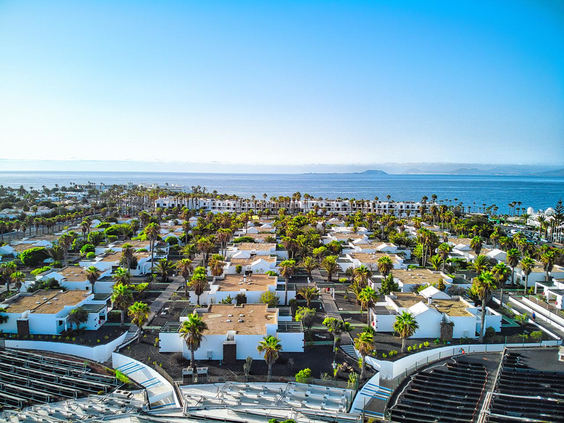 Luchtfoto van de witte bungalows en het zwembad van Relaxia Lanzasur Club op Lanzarote, met de oceaan op de achtergrond.