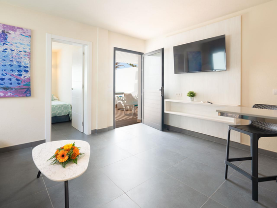 Overzicht van de woonkamer in de bungalow met een zithoek, televisie en doorkijk naar de slaapkamer en het terras.