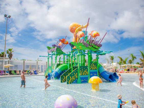 Kinderen spelen in het kleurrijke waterspuitpark van Relaxia Lanzasur Club, met een grote octopus en kleine glijbaantjes.