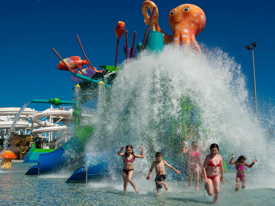 Kinderen staan lachend onder een grote emmer die een waterval van water over hen heen stort in het Aqualava Waterpark.