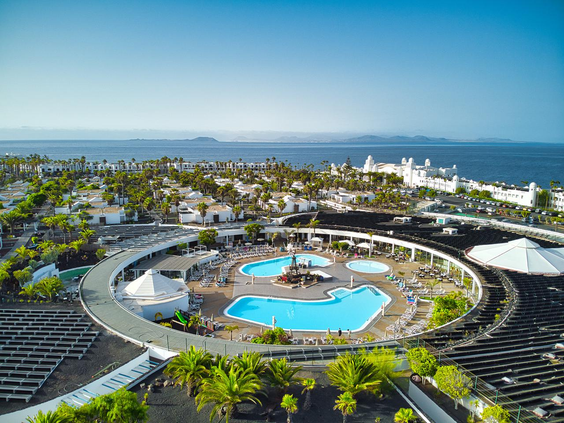 Luchtfoto van het grote, ronde zwembadcomplex van Relaxia Lanzasur Club, met de Atlantische Oceaan op de achtergrond.