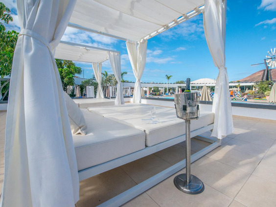 Luxe wit Balinees bed met wapperende gordijnen en een fles champagne in een koeler bij het zwembad.