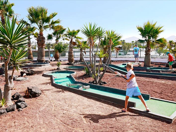 Een jongen speelt op de midgetgolfbaan van Relaxia Lanzasur Club, die is aangelegd tussen palmbomen en vulkanische stenen