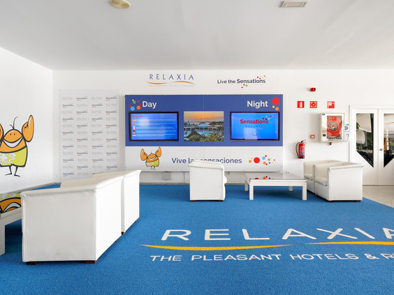 De moderne en kleurrijke ruimte van de kidsclub bij Relaxia Lanzasur Club, met informatieschermen en vrolijke mascottes.