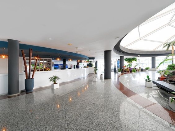 De ruime en lichte lobby van Relaxia Lanzasur Club met een moderne receptiebalie, glimmende terrazzovloer en een groot dakraam.