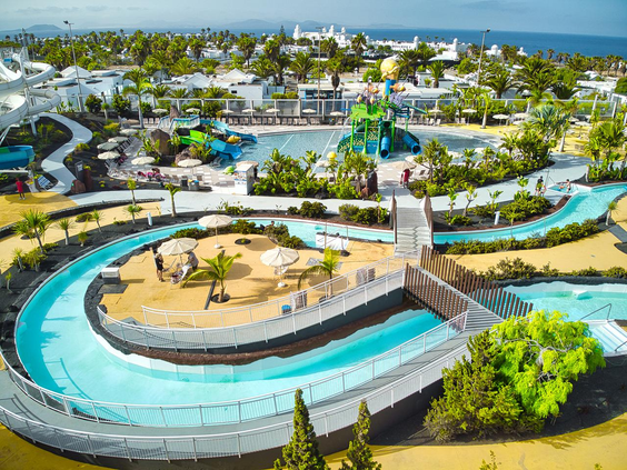 Bezoekers dobberen op een band in de lazy river van het Aqualava Waterpark, omringd door palmbomen.