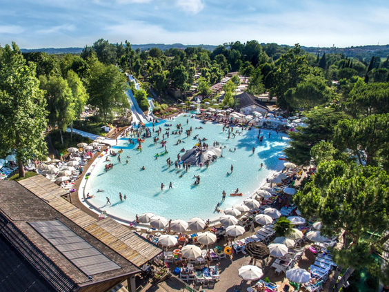 Overzicht van het grote lagune zwembadcomplex op Camping Altomincio Family Park aan het Gardameer, vol met zwemmende gezinnen en omringd door ligbedden en bomen.