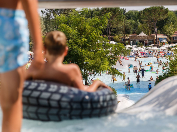 Kinderen op een opblaasband die van een brede waterglijbaan afglijden in het zwembad van Camping Altomincio Family Park.
