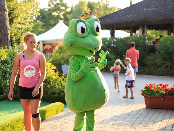 De groene kikker mascotte van Camping Altomincio Family Park begroet lachende kinderen samen met het animatieteam.