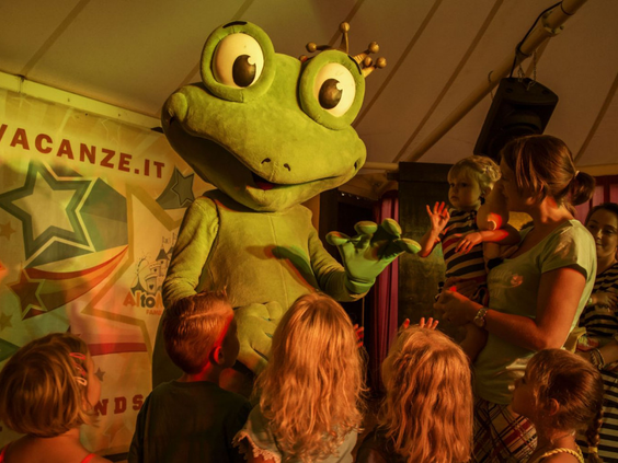 Kinderen kijken naar de kikker mascotte op het podium tijdens de minidisco in de avond op Camping Altomincio Family Park.