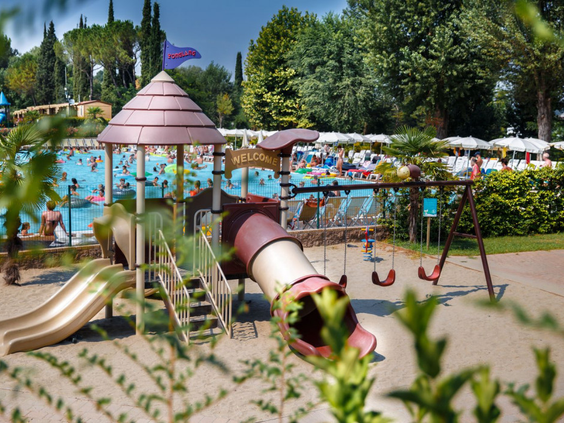 Een speeltuin met glijbaan en schommels direct naast het drukke zwembad op Camping Altomincio Family Park.