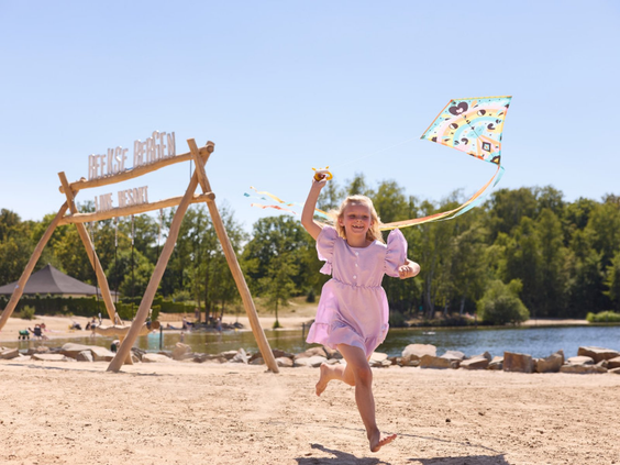 Een meisje rent met een vlieger over het zandstrand bij het Victoriameer op Vakantiepark Beekse Bergen.