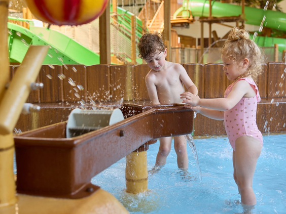 Twee jonge kinderen spelen met een watertafel en sproeiers in het kindergedeelte van het overdekte Junglebad.
