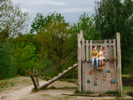 Twee kinderen zitten bovenop een houten klimtoestel in een avontuurlijke speeltuin op Camping Beekse Bergen.