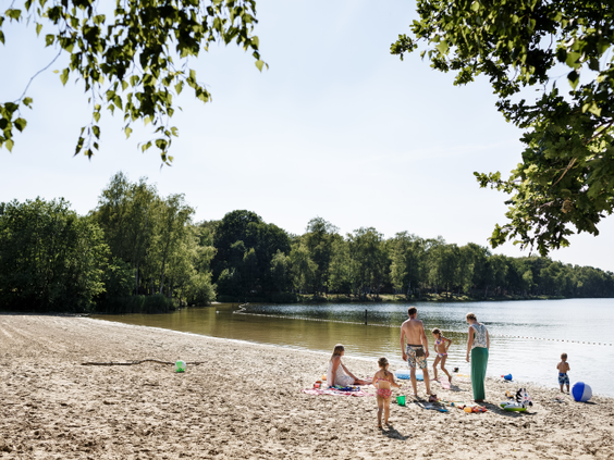 Kinderen en gezinnen genieten van een zonnige dag op het zandstrand aan het Victoriameer op Camping Beekse Bergen.