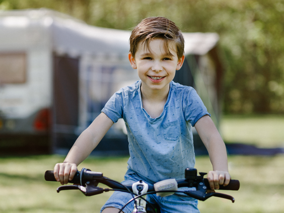 Een lachende jongen fietst op zijn fiets over de groene camping Beekse Bergen.