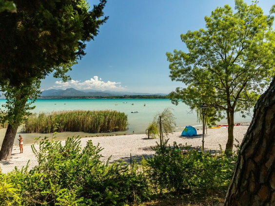 Het zandstrand van camping Bella Italia direct gelegen aan het helderblauwe water van het Gardameer.