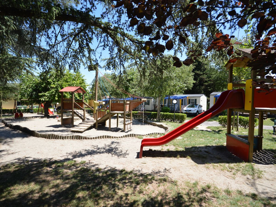 Speeltuin met glijbanen onder schaduwrijke bomen Camping Bella Italia kindvriendelijk
