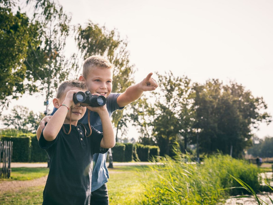 Twee jongens kijken met een verrekijker naar de natuur op het terrein van Camping de Schatberg.