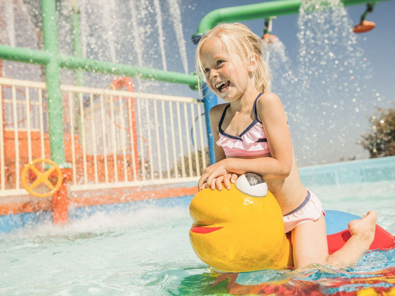 Meisje heeft plezier in het spraypark met een geel waterelement op Camping de Schatberg.