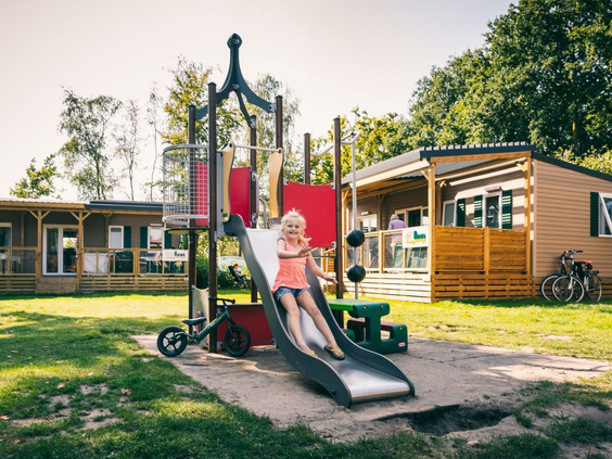 Meisje glijdt van een glijbaan in een speeltuin tussen de chalets op Camping de Schatberg.